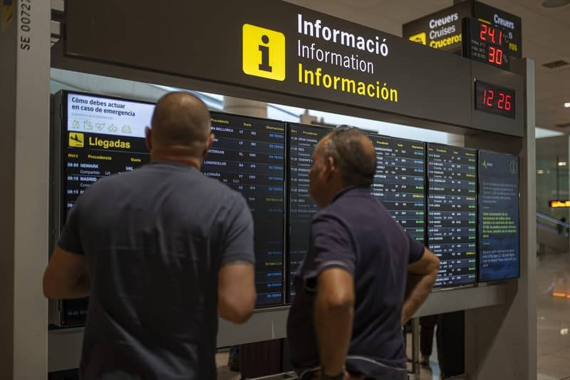 Varias personas observan un panel de llegadas en el aeropuerto de Barcelona