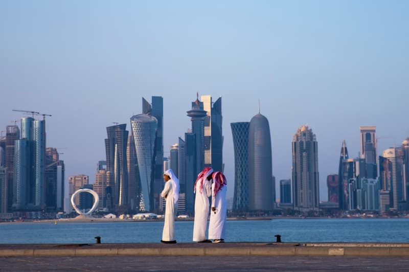 Tres homes caminen davant l'skyline de Doha