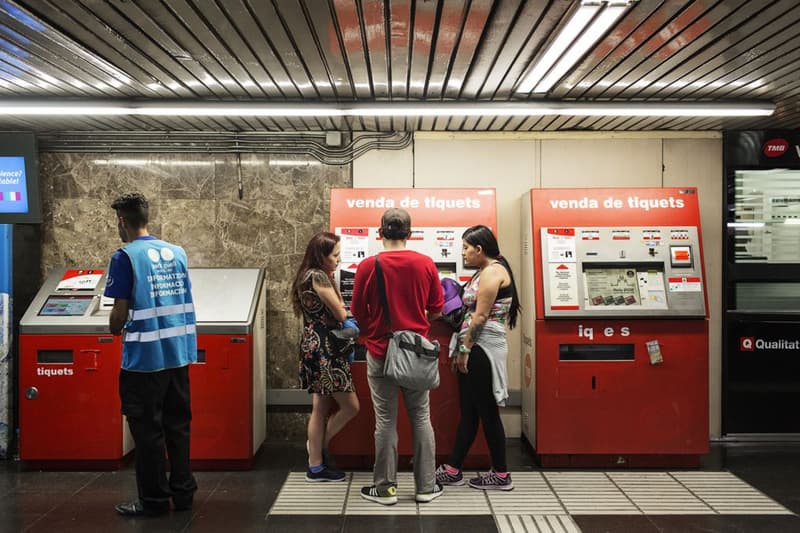 Máquinas de venta de tickets en el metro con personas comprando y un informador al lado