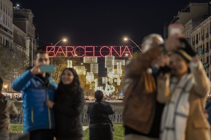 Gente fotografiándose en la gran vía de las Corts Catalanas delante del letrero “Barcelona” de las luces de Navidad
