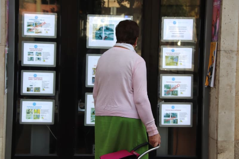 Una mujer revisa las ofertas de pisos en venta fuera de una inmobiliaria.