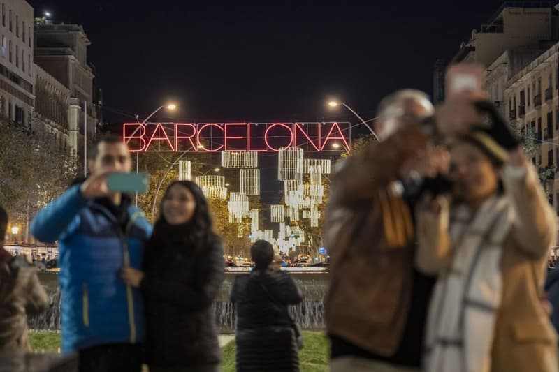 Gente fotografiándose en la gran vía de Les Corts Catalanes ante el rótulo “Barcelona” de las luces de Navidad